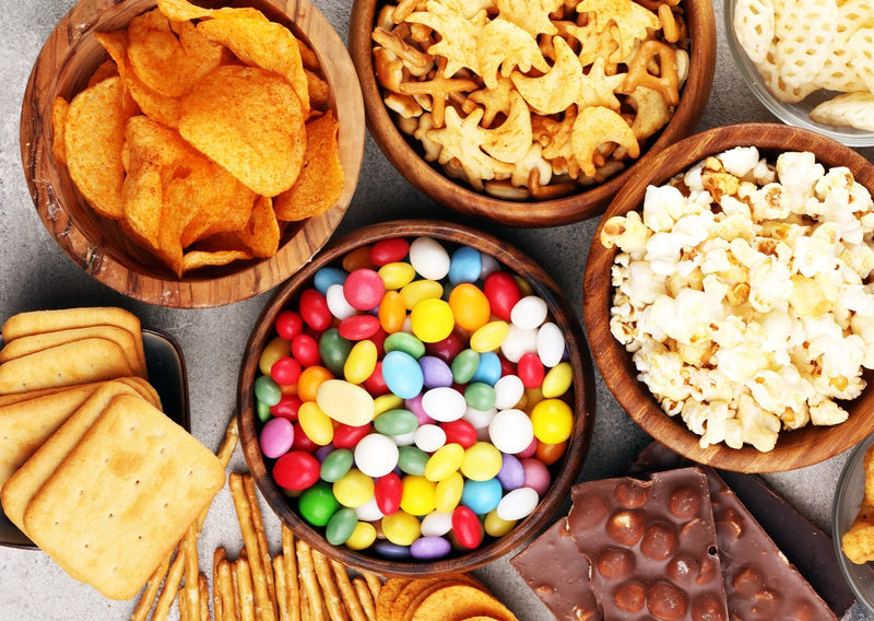 An overhead view of small dishes holding a variety of snacks, including chips, candies, popcorn, cookies, and crackers.